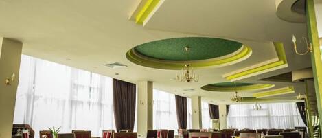 Un restaurante con mesas redondas, sillas tapizadas en rojo y un diseño de techo circular verde.