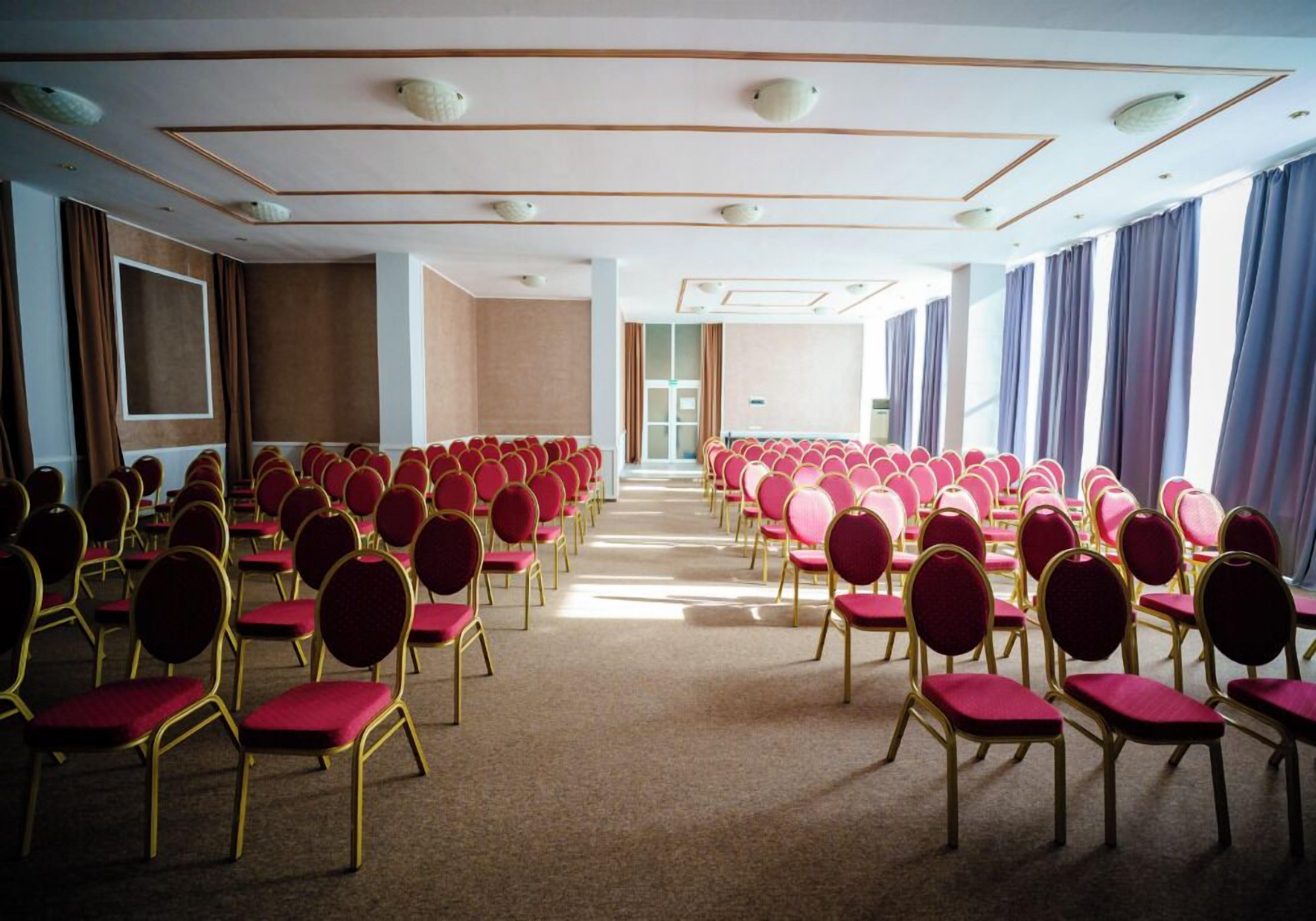 Un salón de conferencias con filas de sillas rojas y suelo alfombrado.