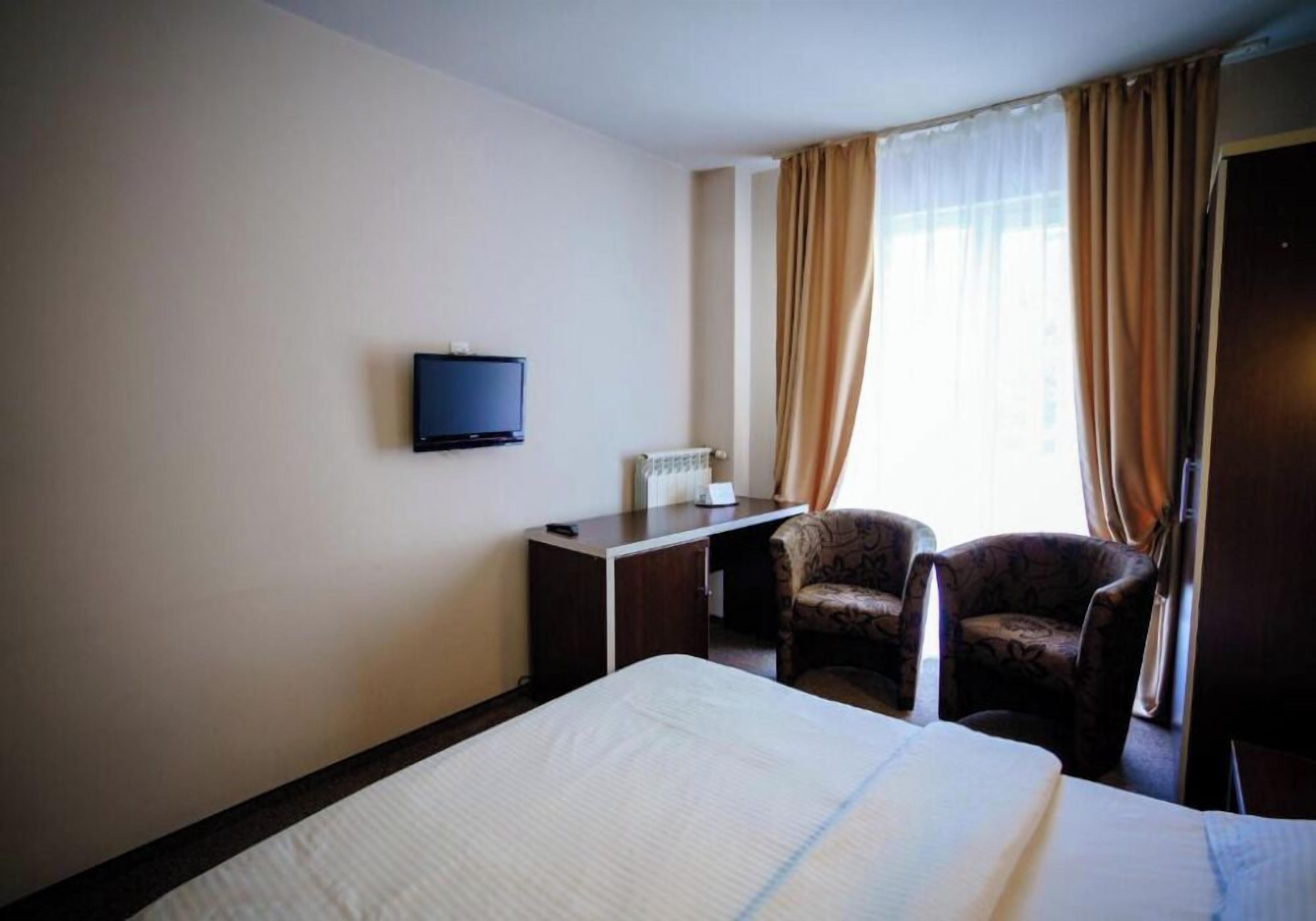 Una habitación de hotel con cama, escritorio con televisor, silla y ventana con cortinas.