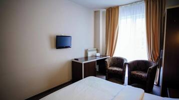 Una habitación de hotel con cama, escritorio con televisor, silla y ventana con cortinas.