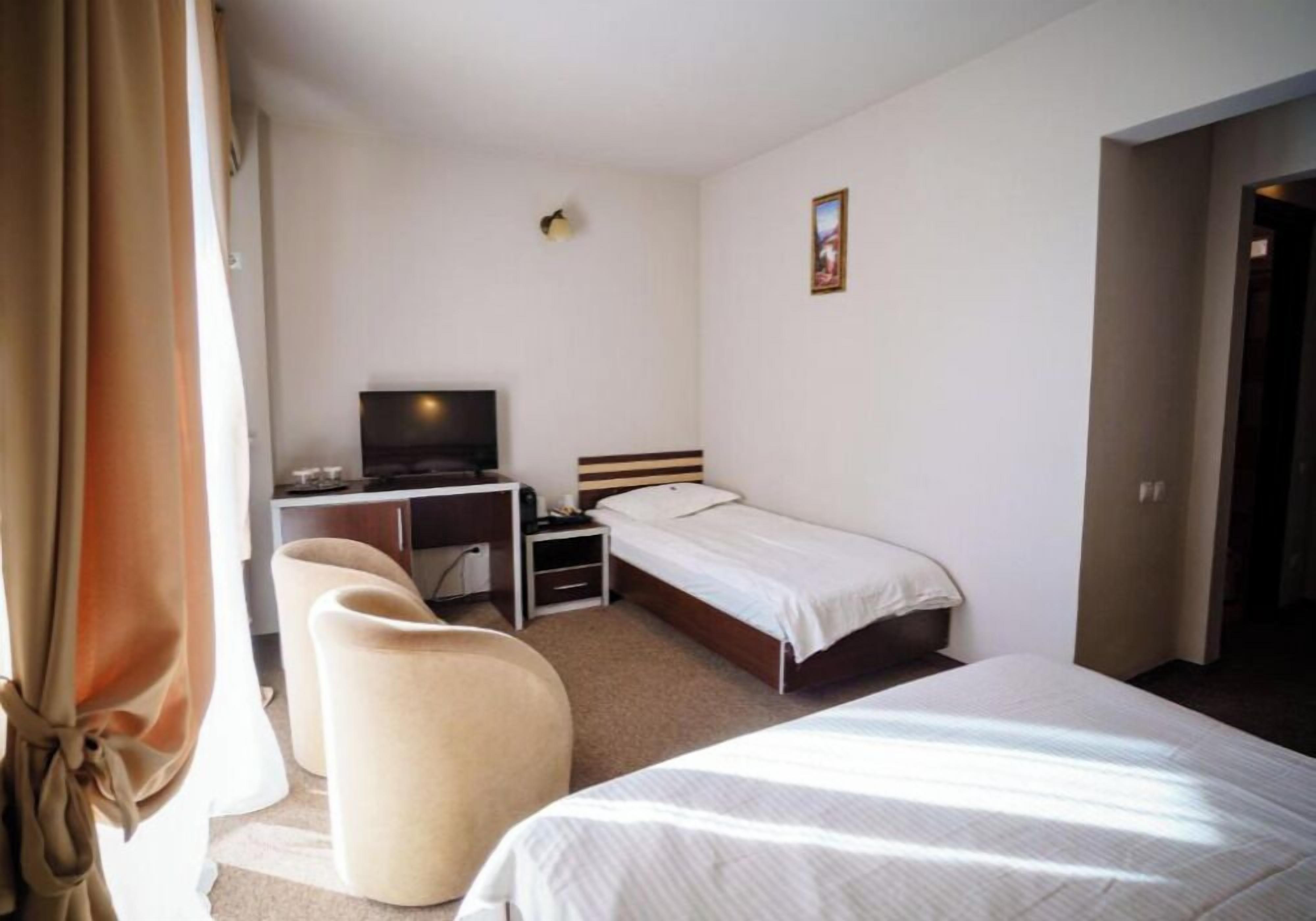 A hotel room with a bed, a desk with a television, a chair, and a small bedside table.