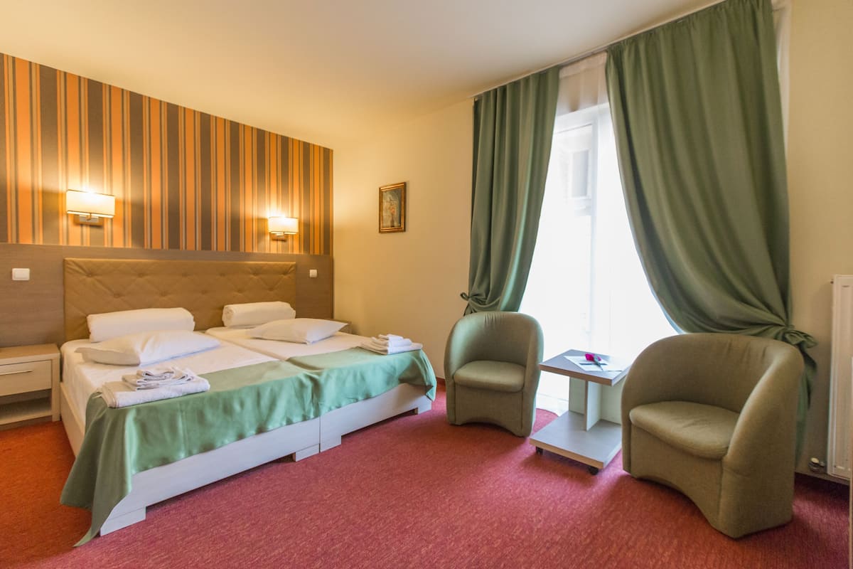 A hotel room with a bed, two armchairs, a small table, a lamp, and a painting on the wall.