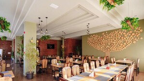 A spacious dining area with multiple tables and chairs, a brick wall, hanging plants, and a unique wooden wall art piece. - Diana Resort (Baile Herculane)
