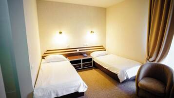 Ein Hotelzimmer mit zwei Einzelbetten, einem Holzkopfende, einem kleinen Tisch, einem Stuhl und zwei Wandleuchten.