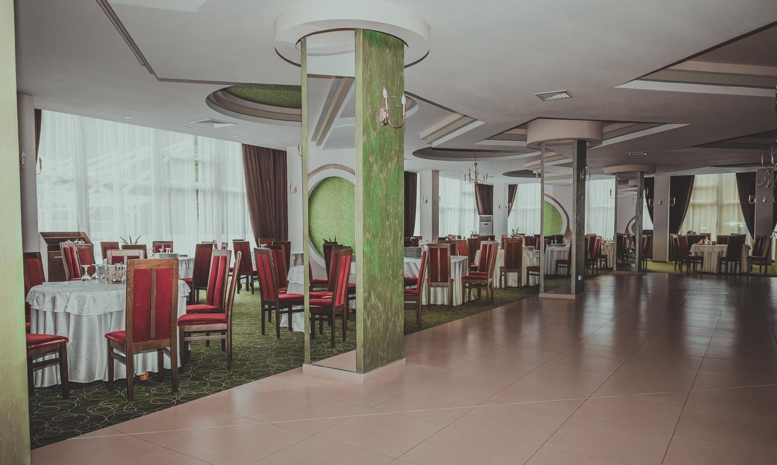 Un vaste espace dédié à la salle à manger, avec de nombreuses tables et chaises, de grandes fenêtres et un mur d’accent de couleur verte.