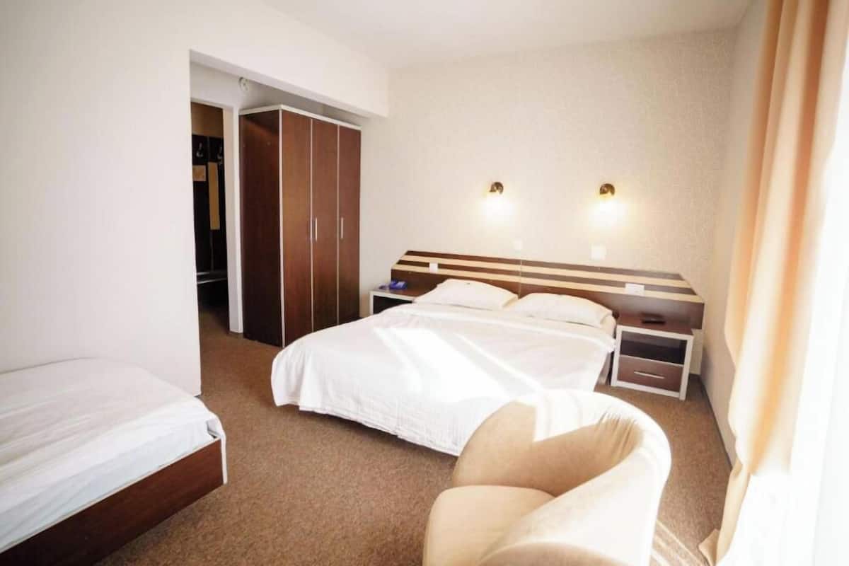 A hotel room with a bed, a chair, a wardrobe, and two wall-mounted lights.