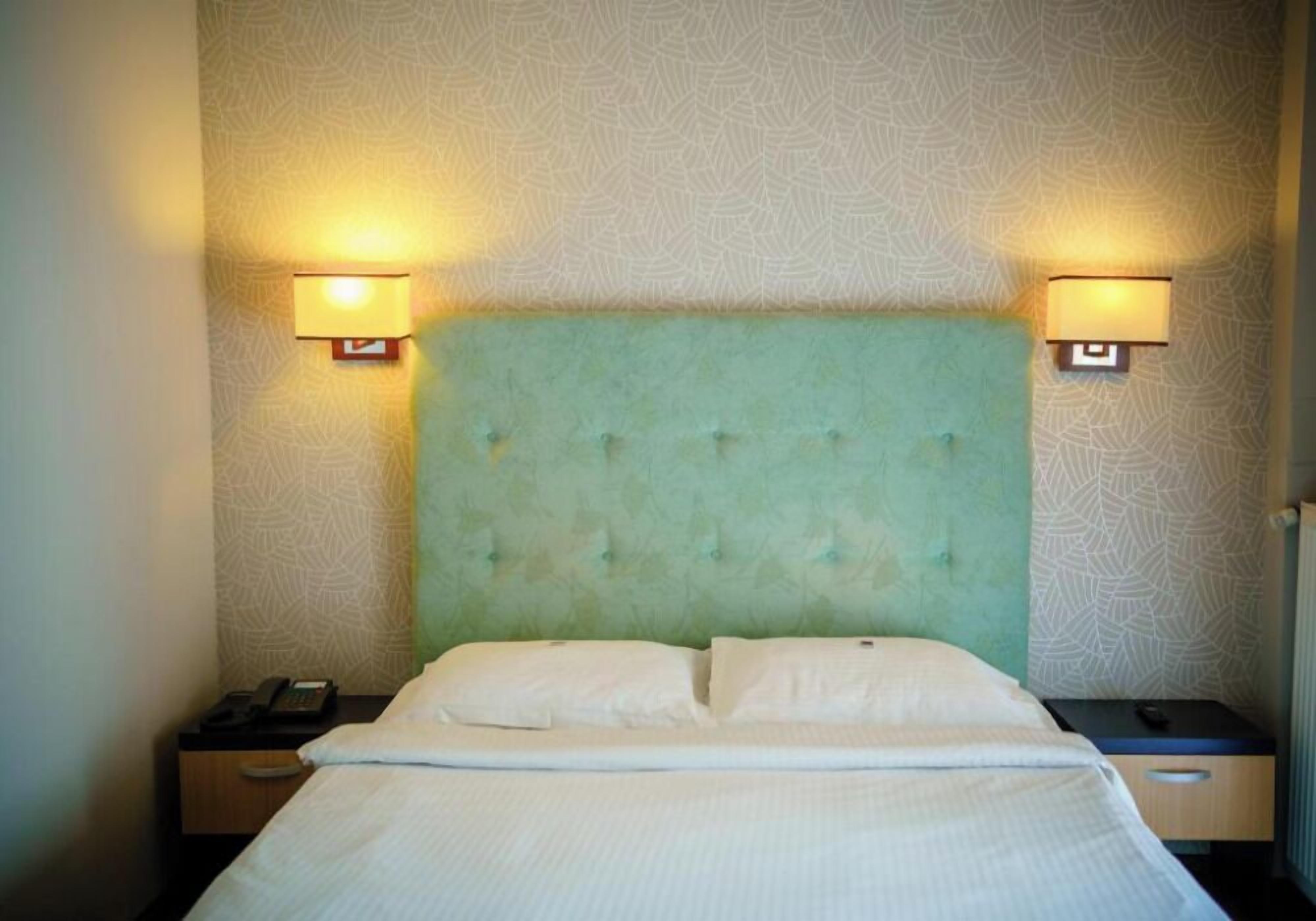 A hotel room with a tufted headboard, two bedside lamps, a telephone, and a drawer.