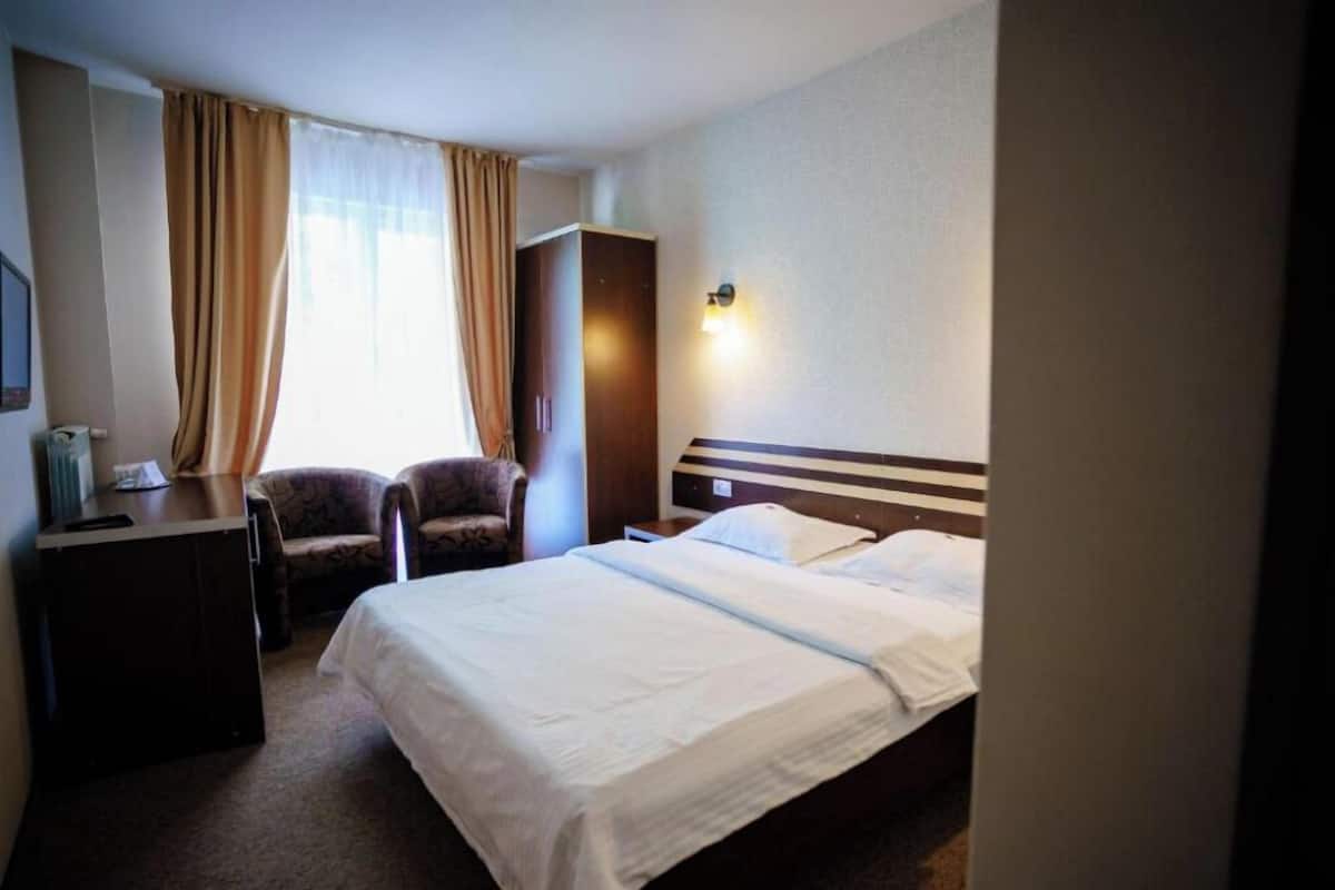 A hotel room with a bed, a desk, a chair, a wardrobe, and a nightstand.
