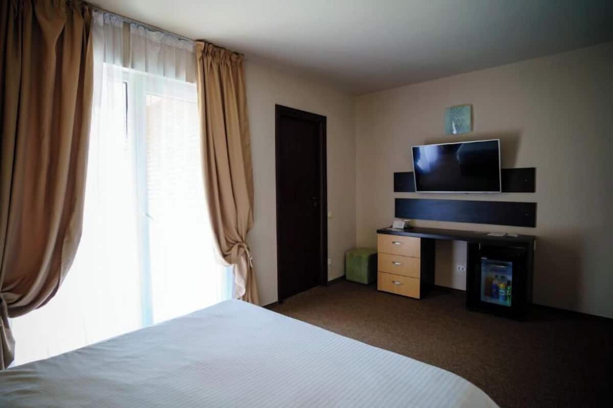 A hotel room with a bed, a TV, a desk with drawers, and a door.
