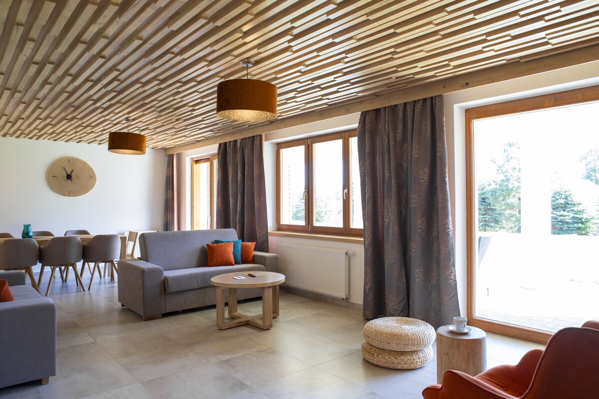 A spacious living area with a modern ceiling design, large windows, and comfortable seating.