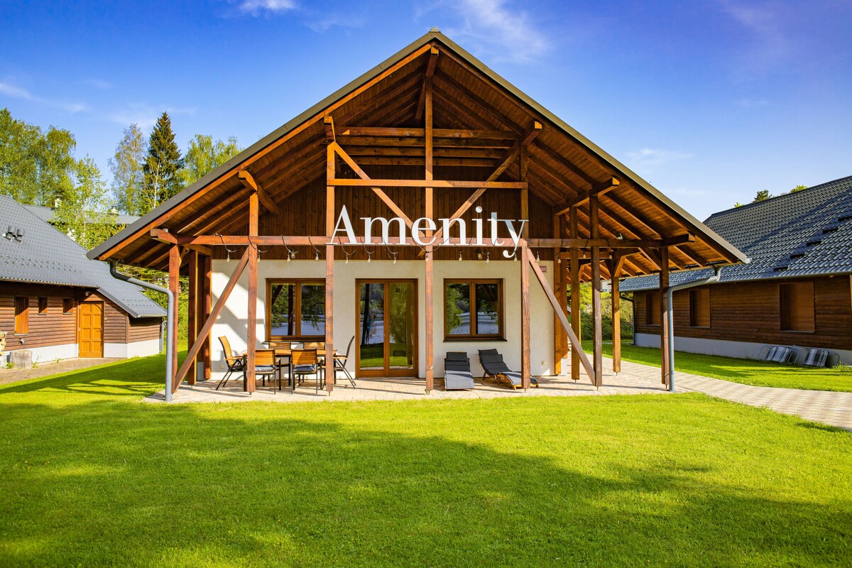 A wooden cabin with a covered patio, large windows, and a well-maintained lawn.