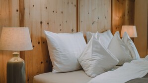 A neatly made bed with white linens and pillows, a wooden headboard, and two bedside lamps. - Warm vacation apartment at Hof Neuhaus (Platzers)