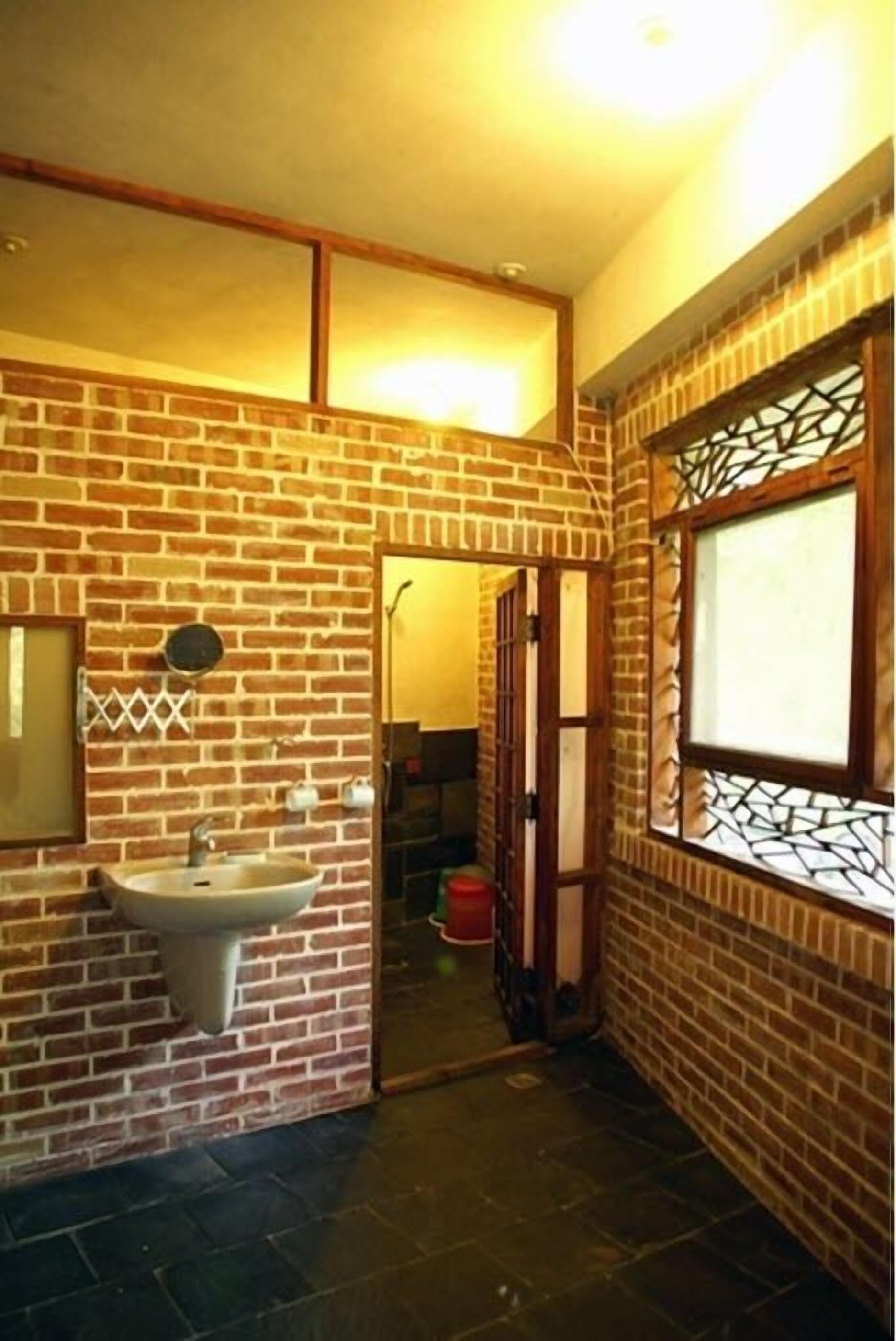 A narrow bathroom with a brick wall, a sink, and a window with a decorative grille.