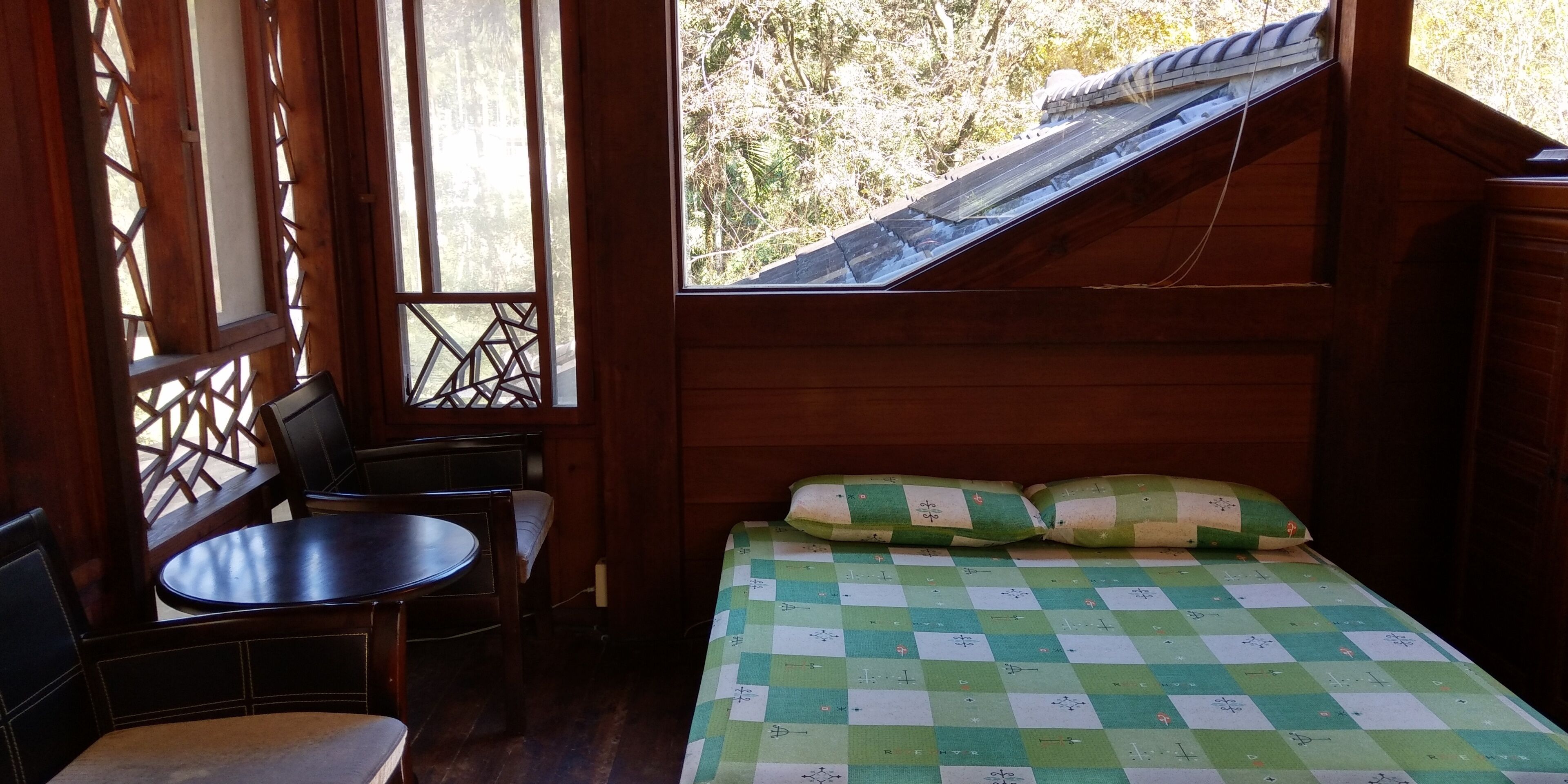 Une pièce avec un lit, une petite table et des chaises. Il y a une fenêtre donnant sur des arbres.