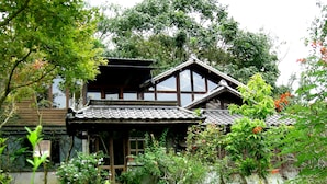A traditional Japanese-style house surrounded by lush greenery and flowering plants. - Water Home (Puli)