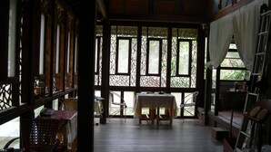 A room with a wooden floor, a table with chairs, and large windows with decorative glass. - Water Home (Puli)