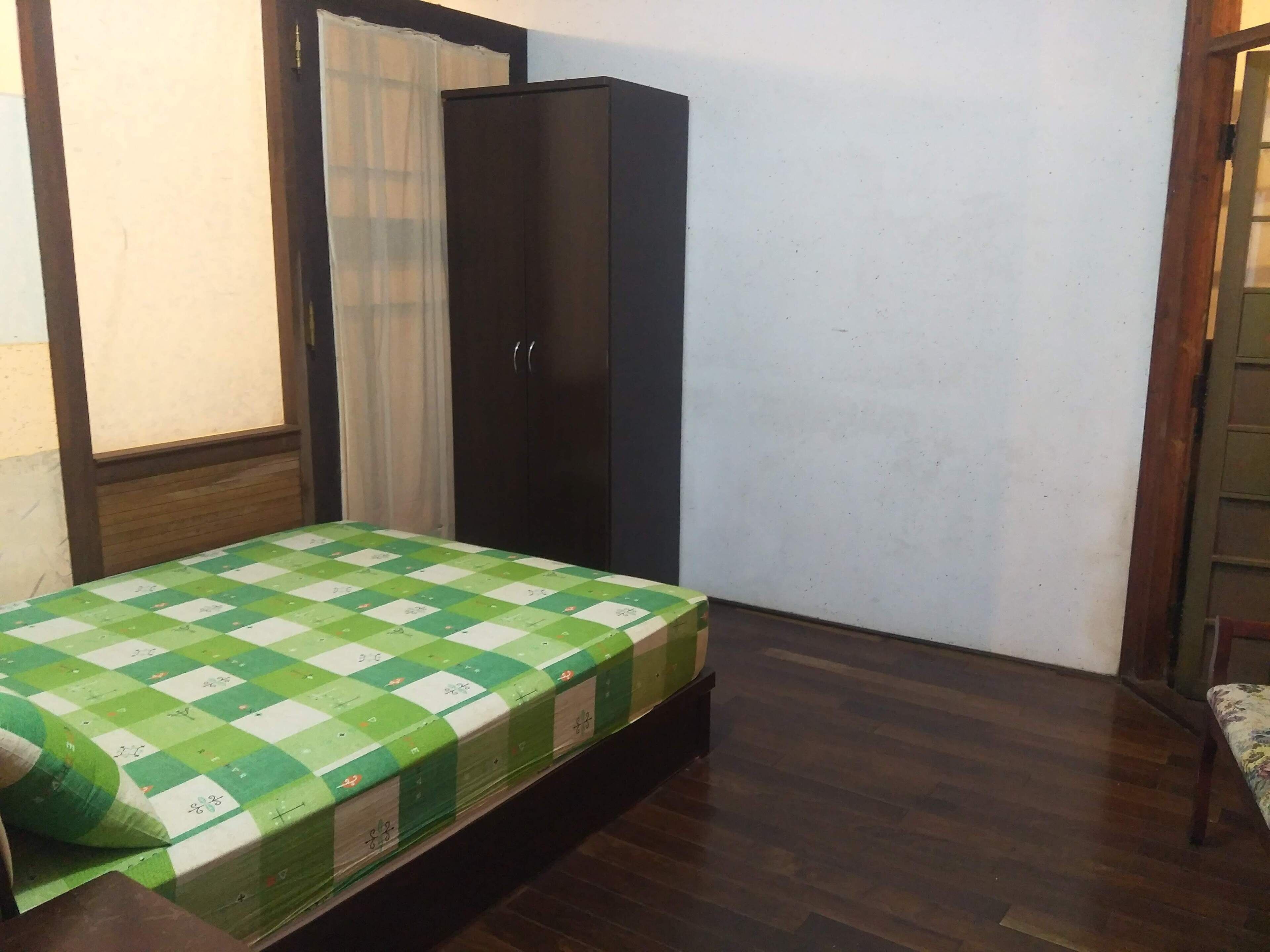Een compacte, keurig ingerichte kamer met een bed, een kast en een raam met gordijnen.