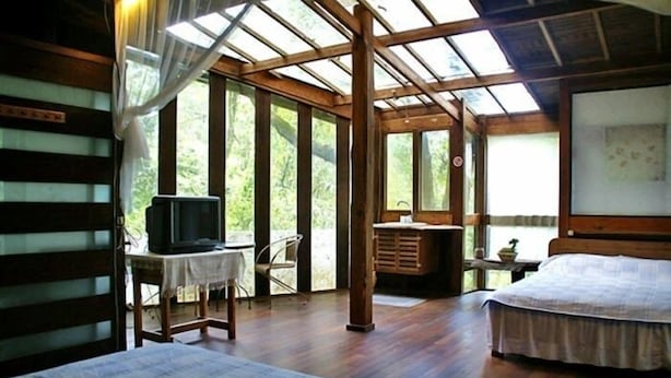 A room with two beds, a desk with a television, and large windows allowing natural light. - Water Home (Puli)