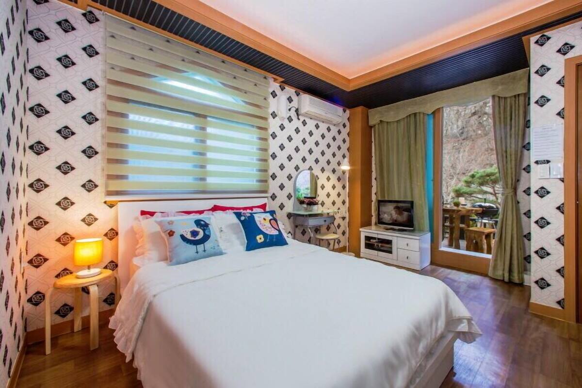 Une chambre à coucher avec un lit, des tables de chevet, une télévision et une fenêtre avec des stores.