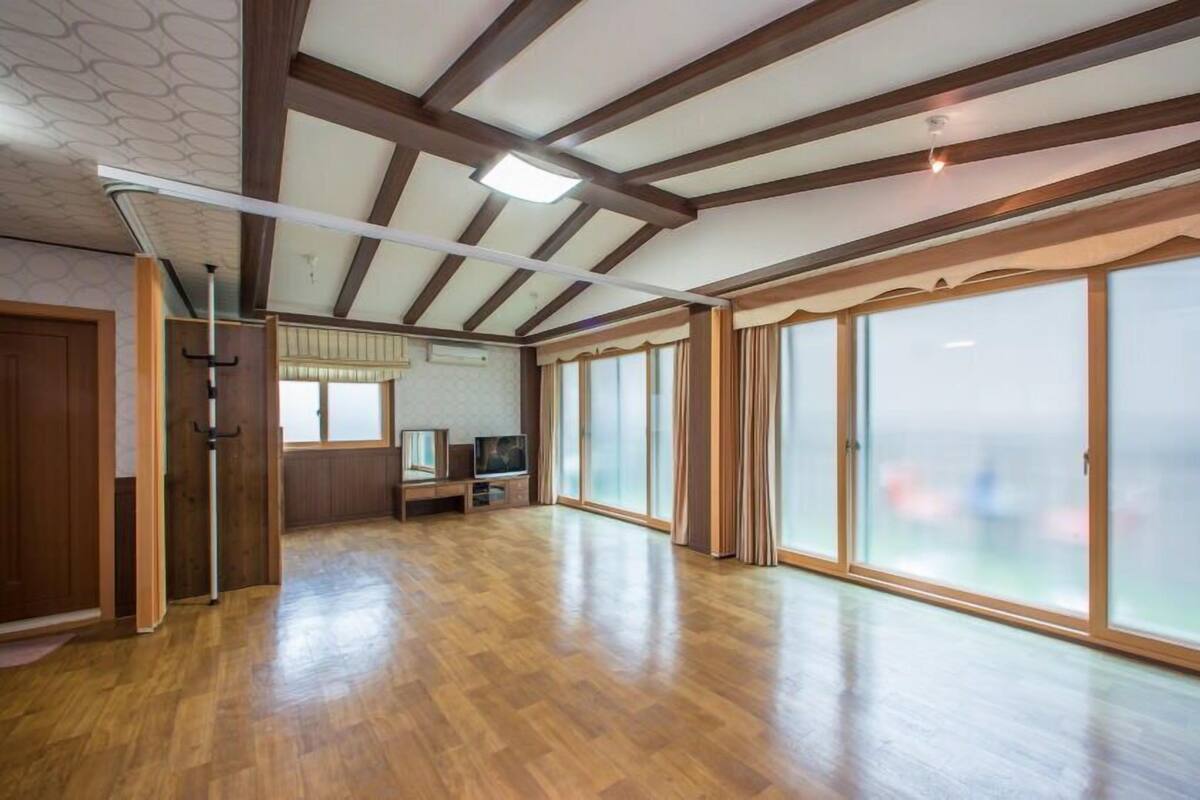 Une pièce spacieuse dotée d’un plancher en bois, d’une grande porte-fenêtre coulissante et d’un plafond avec des poutres apparentes.