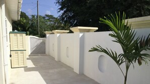 A narrow, enclosed pathway with a potted plant, a white wall with circular cutouts, and a door with shutters. - Private detached villa in a quiet location close to the sea and beaches (Porters)