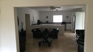A living room with a black leather sofa, a coffee table, and a kitchen in the background. - Private detached villa in a quiet location close to the sea and beaches (Porters)