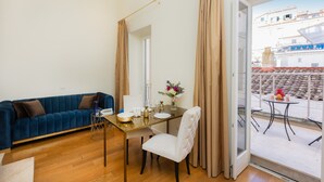 Een woonkamer met een blauwe bank, een witte stoel, een glazen tafel en uitzicht op de stad door een glazen deur.
