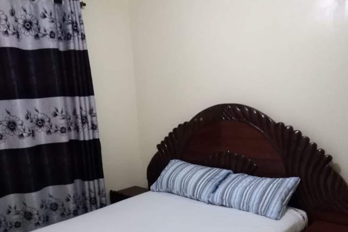 Quarto com cama de madeira, travesseiro listrado, mesa de cabeceira e cortina floral.
