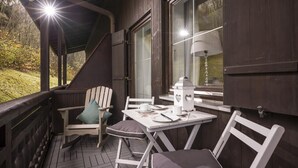 A wooden deck with a table and chairs, a lamp, and a window overlooking a garden. - 2 room apartment in country house still,dishwasher,cozy balcony,13 (Oberaudorf)