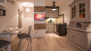 A modern kitchen with wooden flooring, white cabinetry, a television mounted on the wall, and a dining area with a table and chairs. - 2 room apartment in country house still,dishwasher,cozy balcony,13 (Oberaudorf)