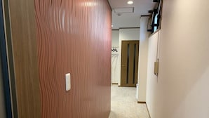 A hallway with a wooden door, a light switch, and a door in the background. - AO-Dazaifu (Chikushino)