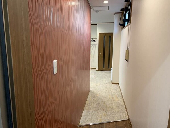 Un pasillo con una puerta de madera, un interruptor de luz y otra puerta al fondo.
