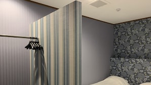 A hotel room with a striped wall, a bed with white bedding, and a floral-patterned headboard. - AO-Dazaifu (Chikushino)
