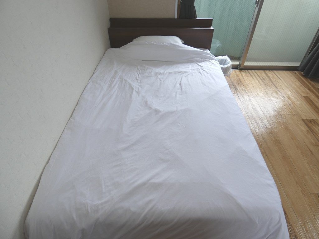 A single bed with white bedding in a room with a wooden floor and a green wall.