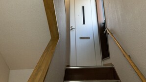 A stairway leading to a white door with a vent above it. - AO-Dazaifu (Chikushino)