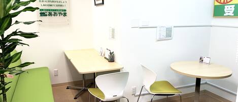 A small office with two tables, chairs, a clock, and a sign on the wall.