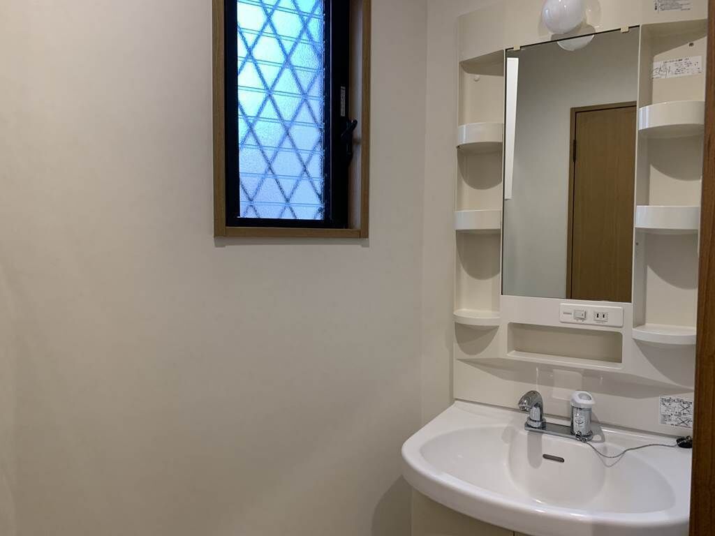 A bathroom with a white sink, a mirror, and a window with a geometric pattern.