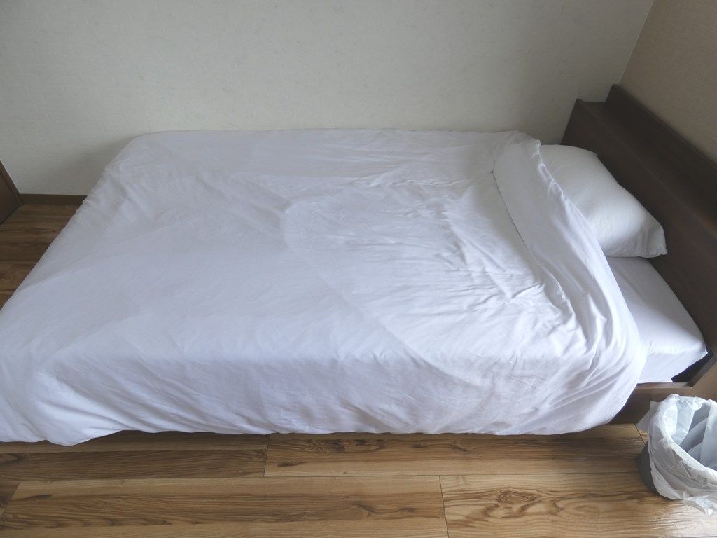 A neatly made bed with white bedding in a room with wooden flooring.
