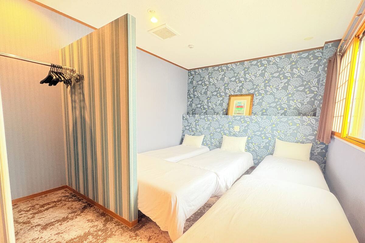 Een hotelkamer met twee bedden, een gestreept scheidingswand, een douchegedeelte en een wand met bloemenmotief.