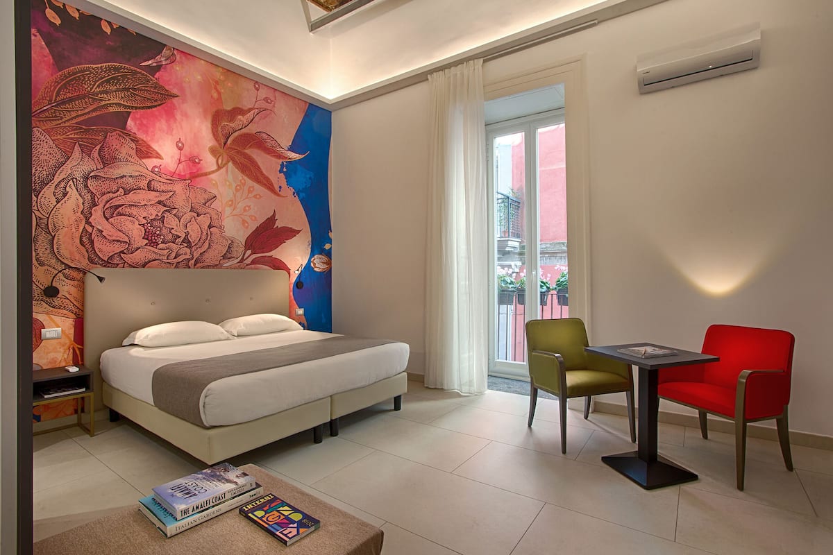 A hotel room with a bed, a desk, a chair, and a large wall mural.