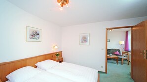 A hotel room with a double bed, a nightstand with a lamp, two framed pictures on the wall, and a view into the adjacent room through an open door. - Zum Alten Brauhaus (Oberwiesenthal)