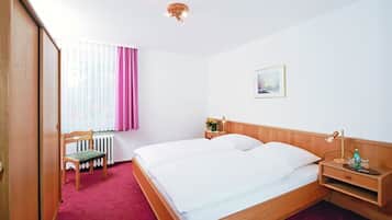 Ein Hotelzimmer mit einem hölzernen Bett, einem Sessel, einem Nachttisch und einem Fenster mit Vorhängen.