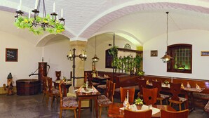 A dining area with wooden tables and chairs, a chandelier, and a stone column. - Zum Alten Brauhaus (Oberwiesenthal)