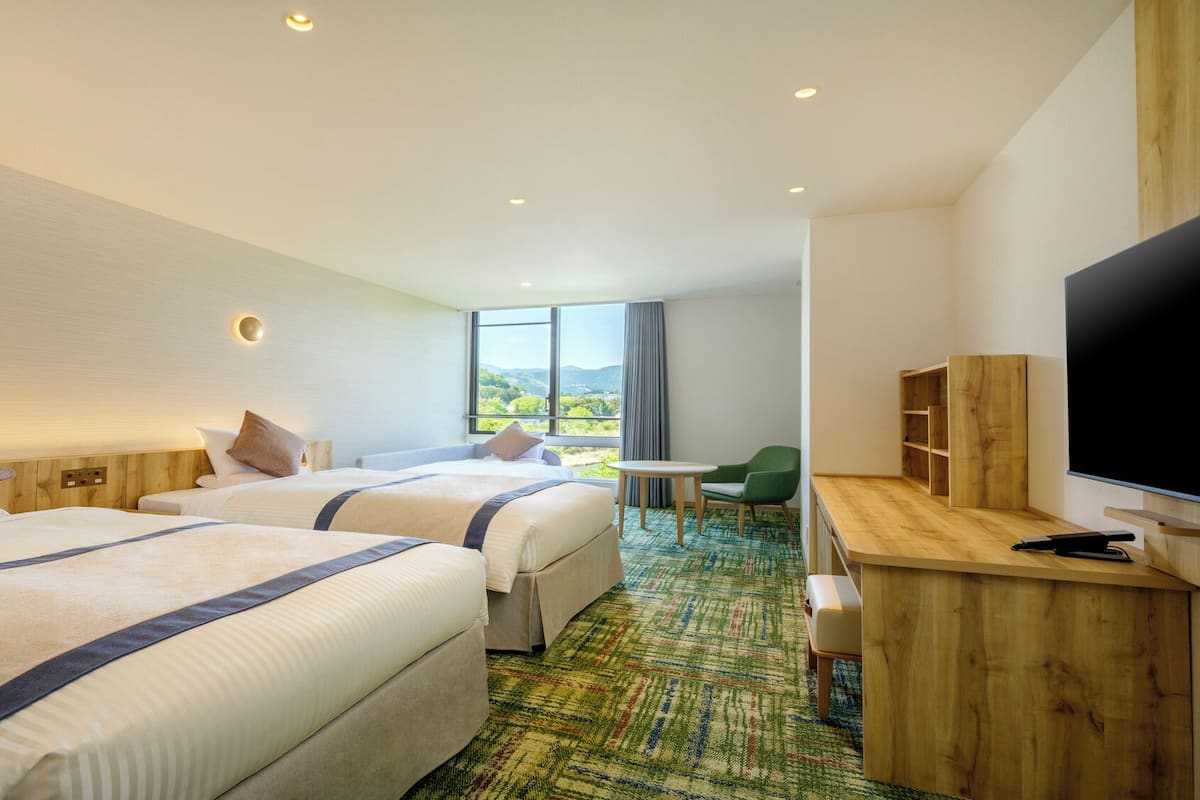A hotel room with two beds, a television, a desk, and a view of the outdoors.