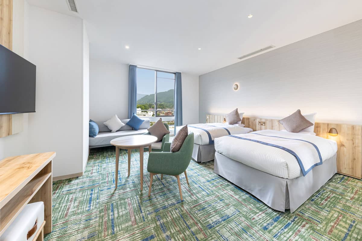 A hotel room with two beds, a sofa, a small table, and a TV.