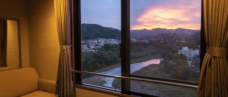 A room with a large window offering a view of a river, a town, and mountains.