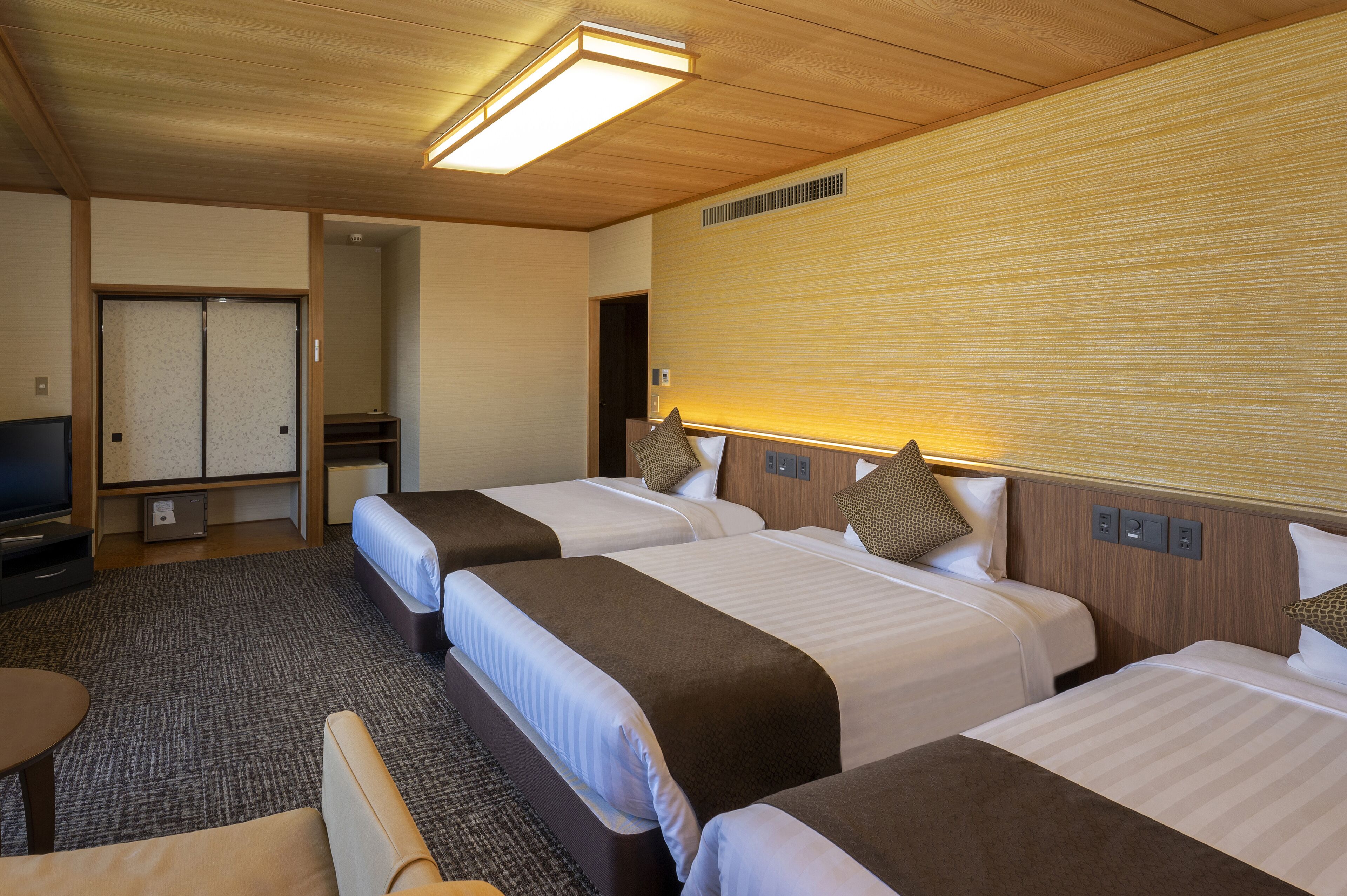 Habitación de hotel con tres camas, televisión, escritorio y piso alfombrado.