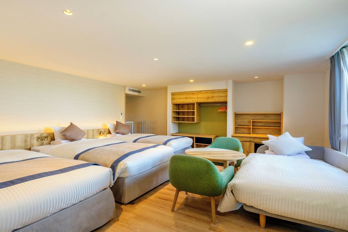 A hotel room with three beds, a small table, and a green chair.