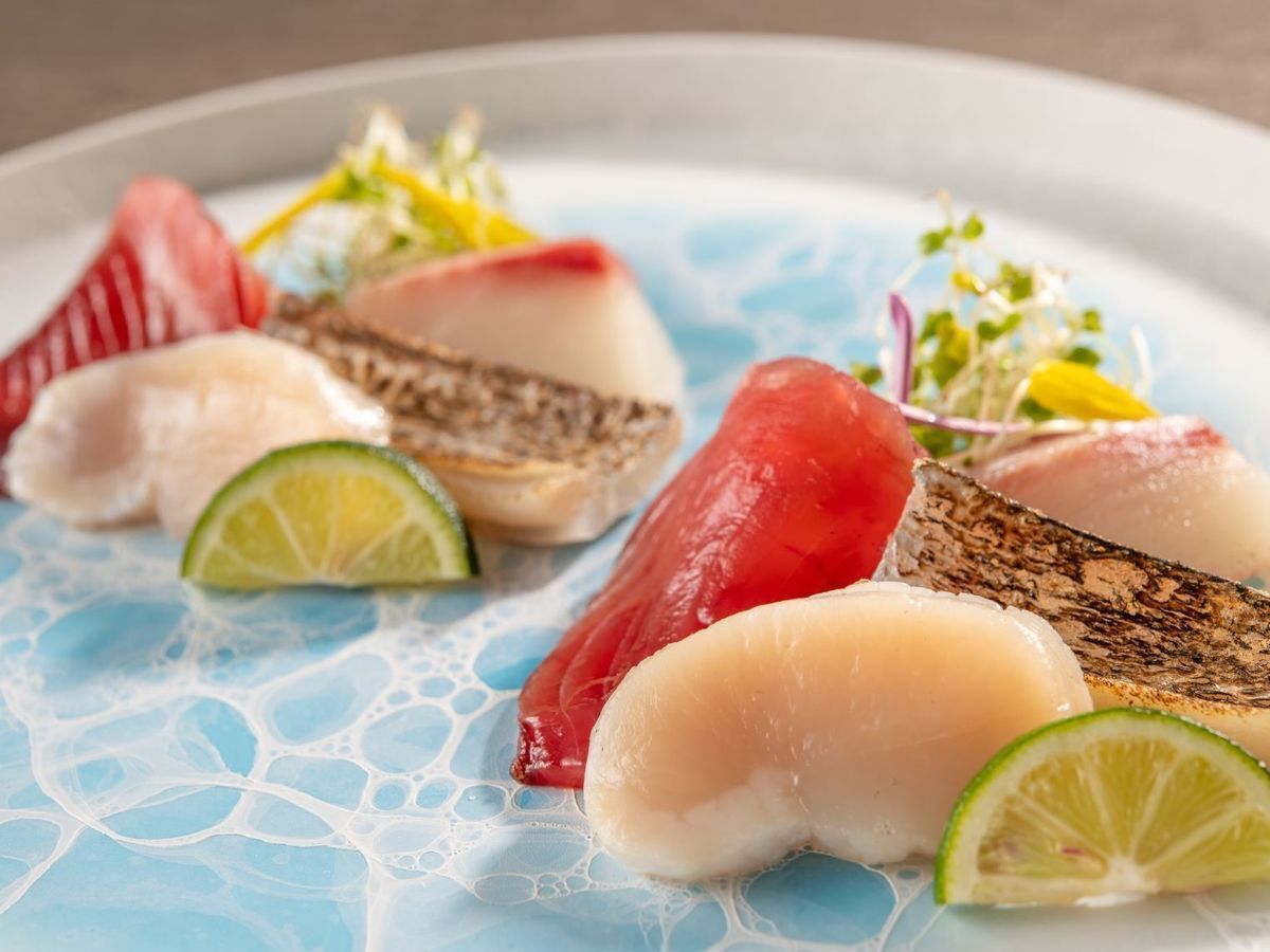 A plate of seafood with lime slices and a blue patterned tablecloth.
