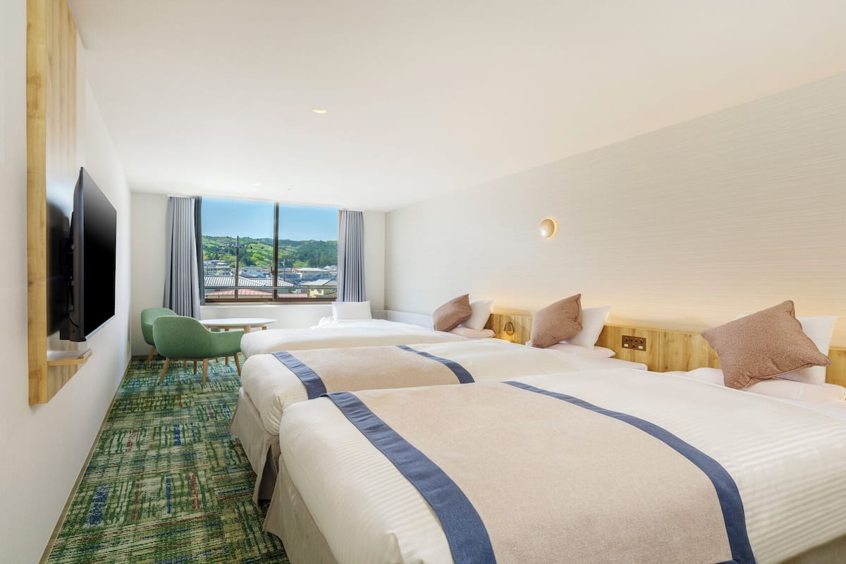 A hotel room with two beds, a TV, a small table, and a view of the city.